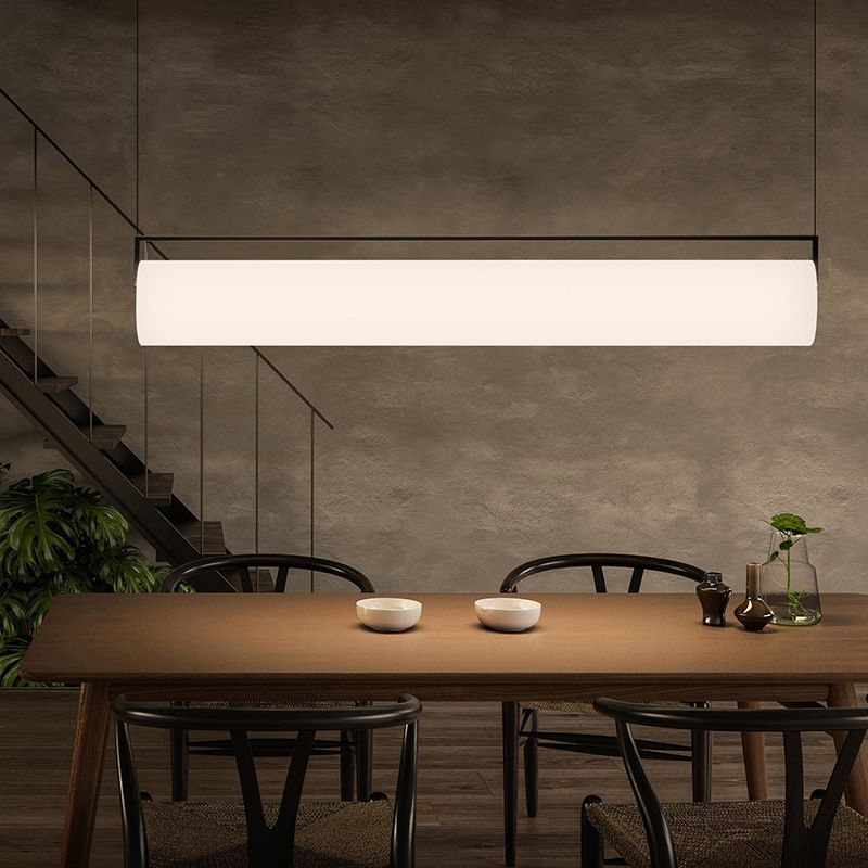 Long white Edge shade and black frame above a dining table in a textured grey interior with plants.