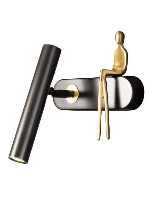 Angled isolated black wall light with tube on the left, gold accent ring and seated figure on the right