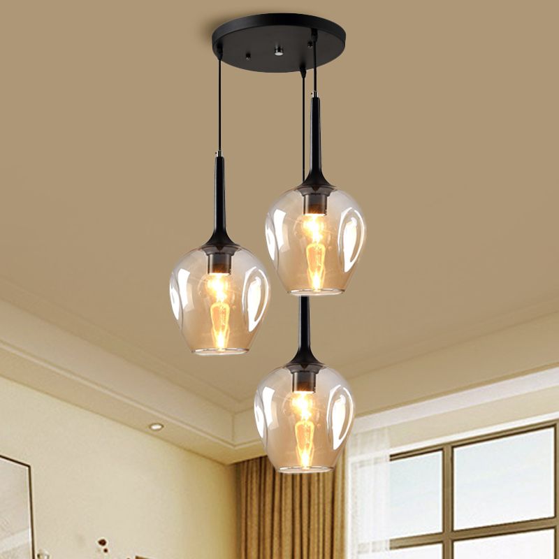 Amber glass cluster pendant with three staggered shades near a window and curtains in a cream room