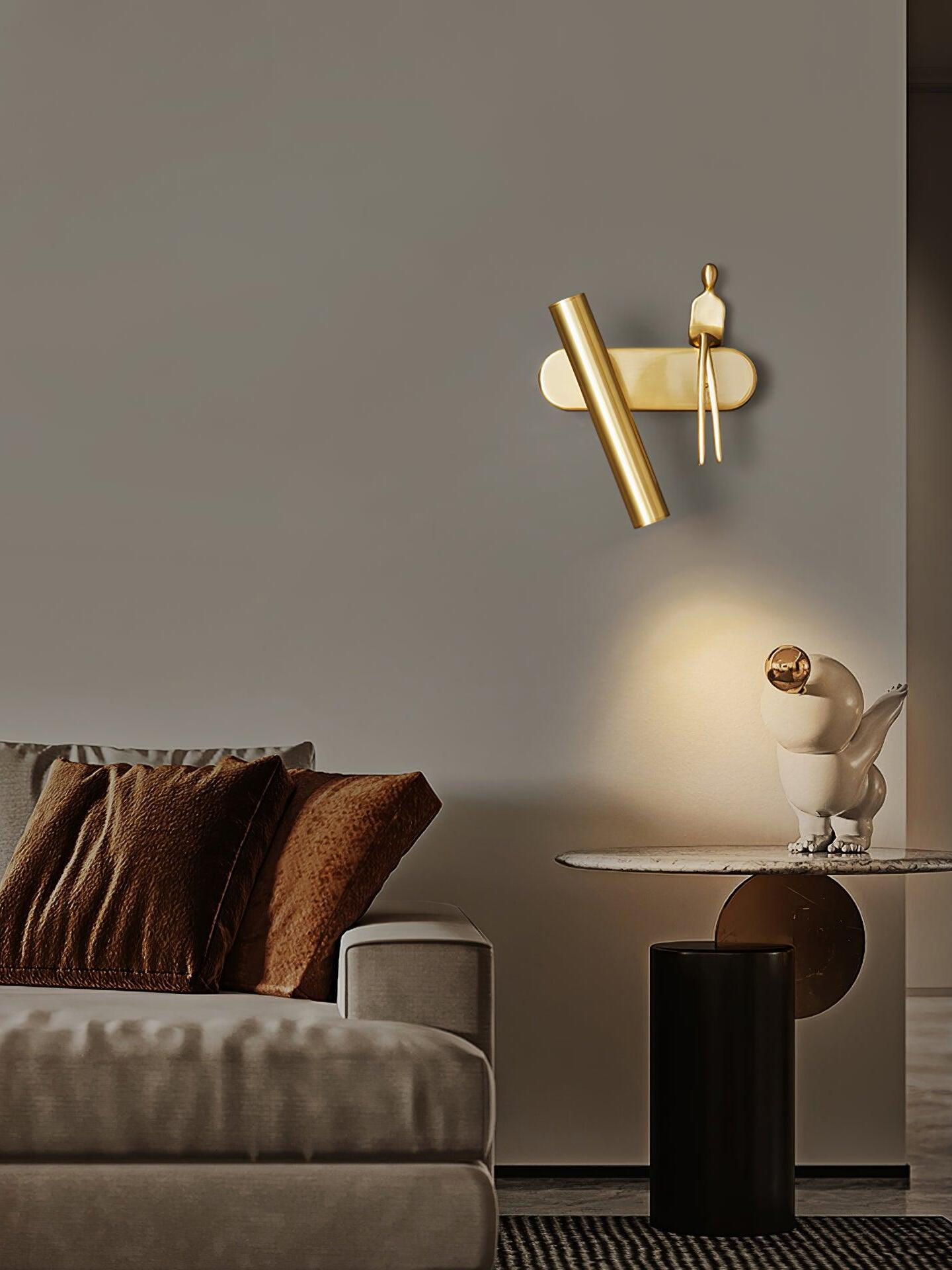 Brass-coloured figure wall light casting light above a sofa and round table with a sculpture