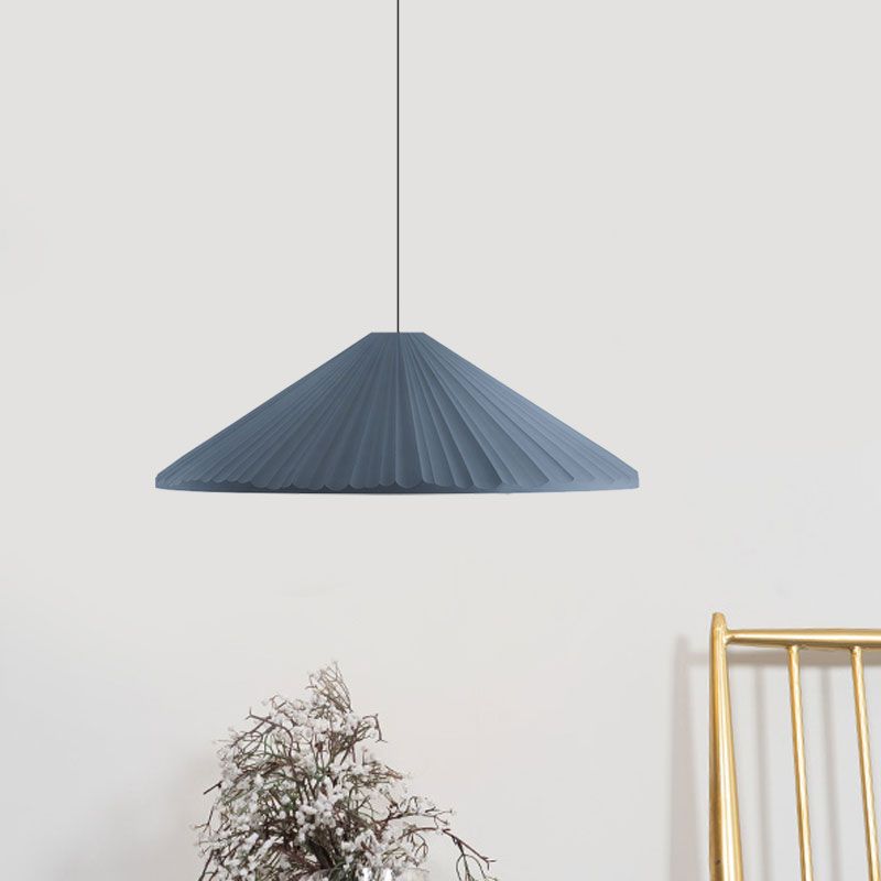 Blue shallow pleated cone pendant near dried flowers and a gold-coloured frame against a white wall
