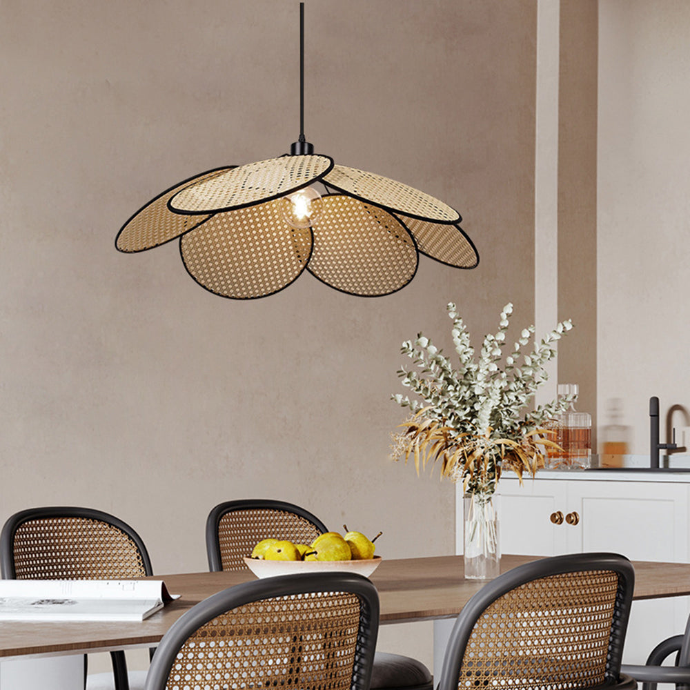 Black-edged woven petal pendant above a wooden dining table with cane chairs, fruit bowl and branch-filled vase