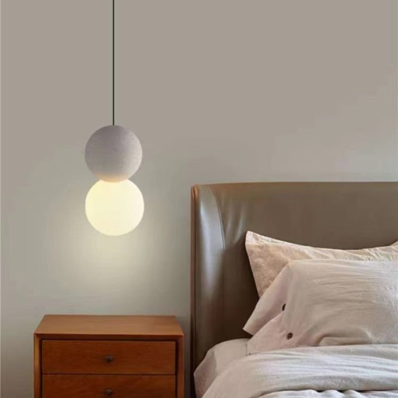 White Byers pendant with a glowing lower globe beside a wooden bedside table.