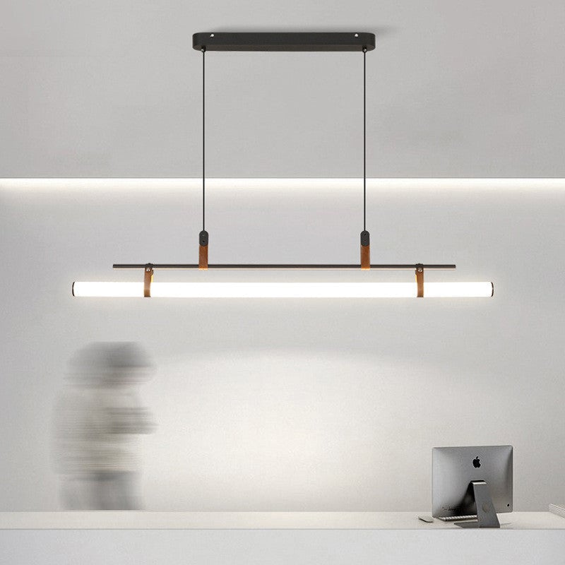 Black linear pendant above a white office counter with a monitor and blurred person, with the ceiling canopy visible