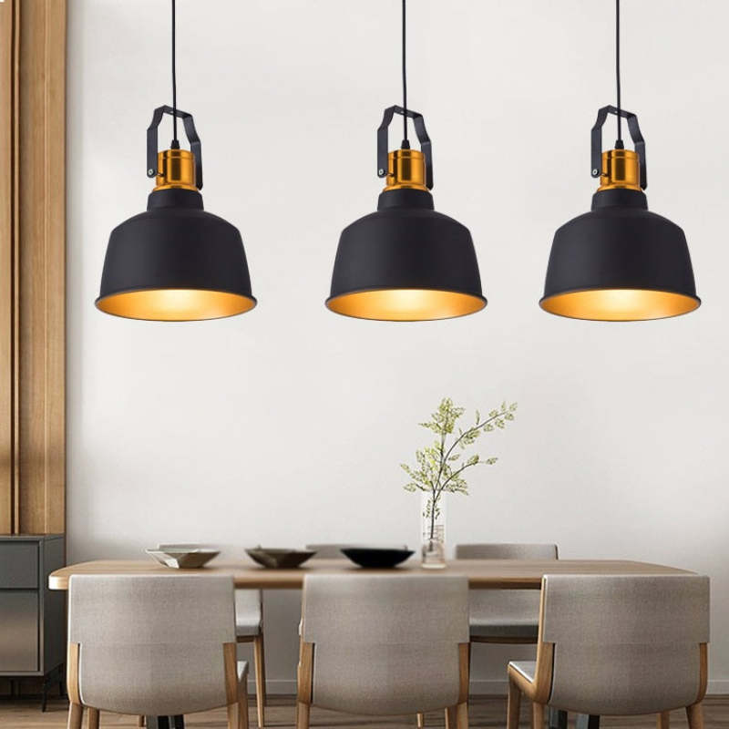 Three separate black dome pendants above a pale wood table with upholstered chairs and a branch-filled vase