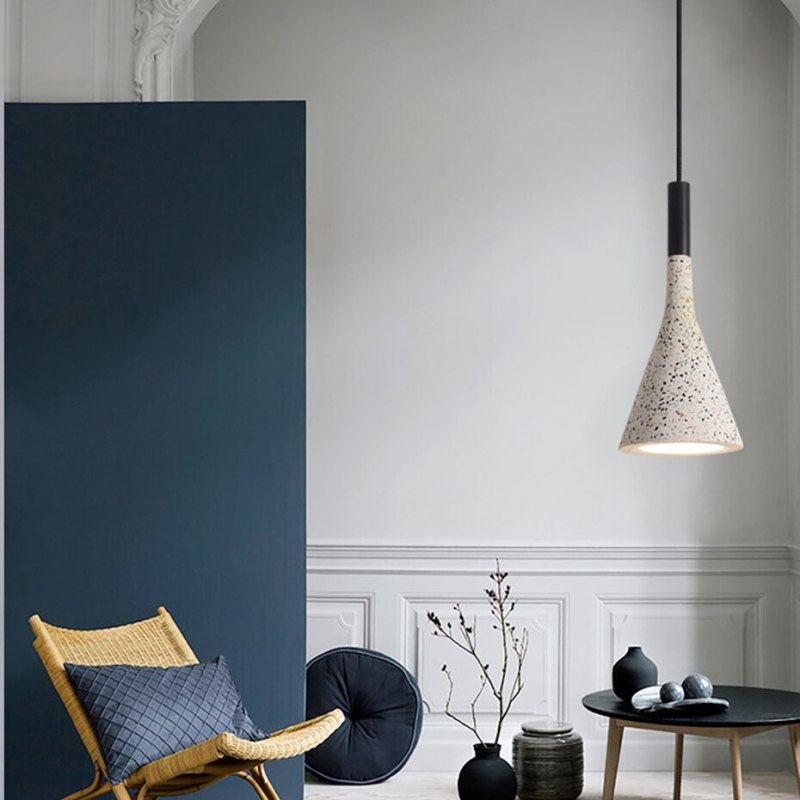 Tall speckled cone pendant with a black upper fitting beside a woven chair and black table