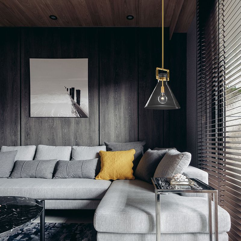 Cairns clear glass cone pendant beside a grey sectional sofa and yellow cushion against a dark wood wall