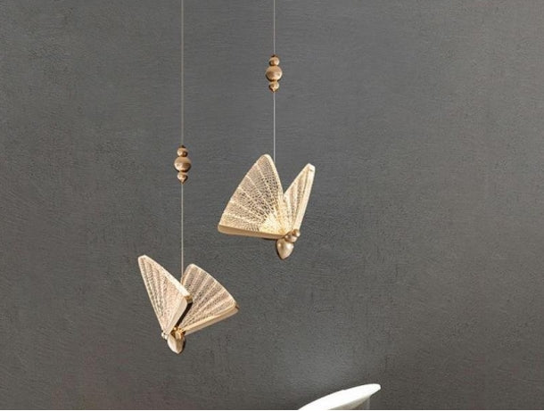 Two gold Kady butterfly pendants against a gray wall