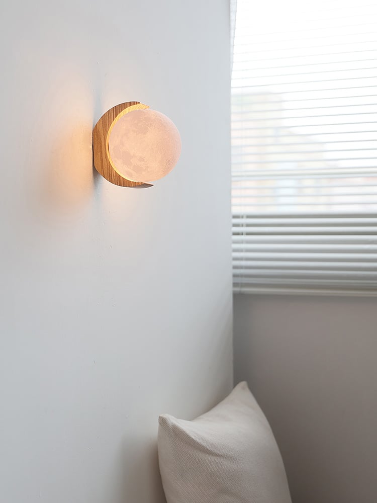 Warm illuminated moon globe and crescent wood bracket above a cushion near window blinds