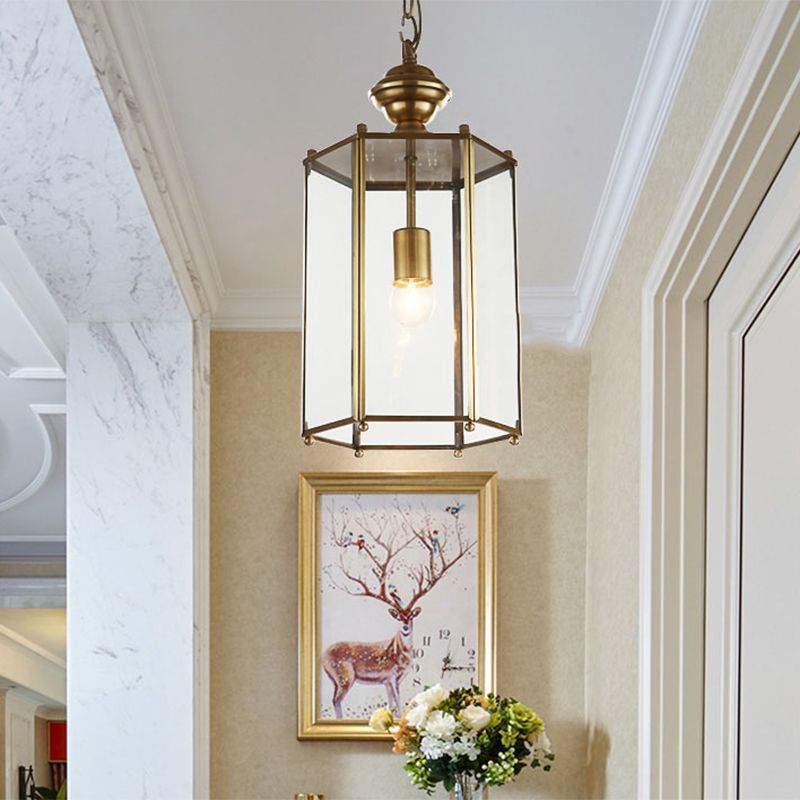 Brass-tone Sanna glass lantern hanging beside framed art and flowers.
