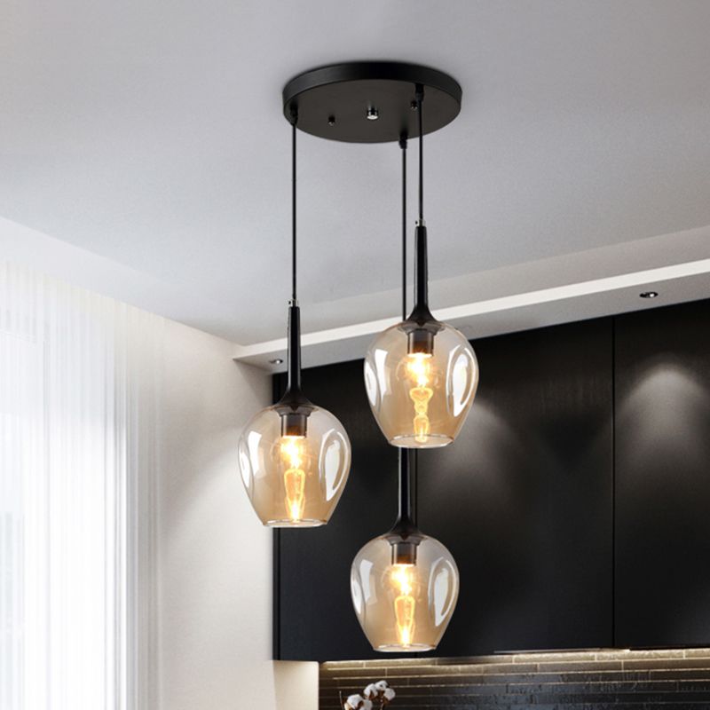 Amber-tinted glass cluster pendant with three lit shades beneath a black canopy in a room with dark wall panels