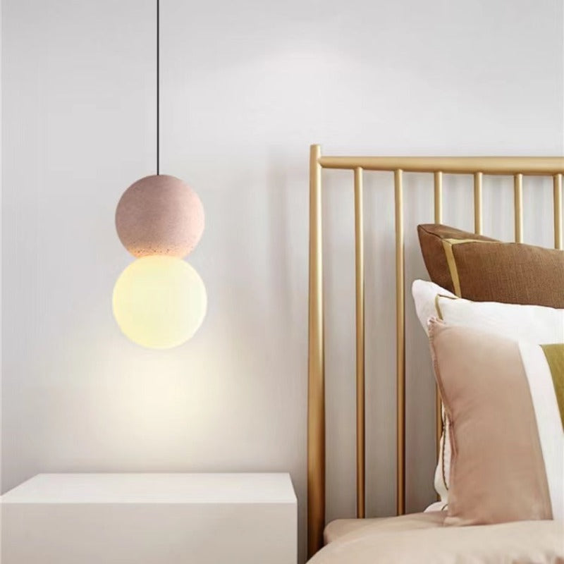 Pink Byers pendant glowing beside a bed with a timber headboard.