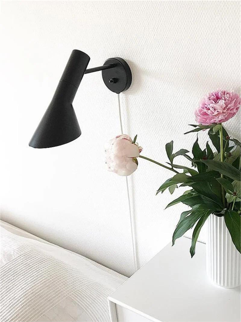 Calix black wall lamp above a white bedside surface and flowers