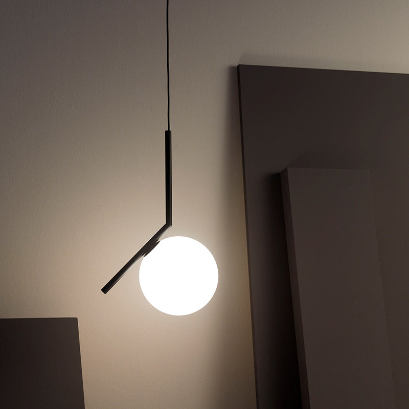 Valentina angular black stem and diagonal arm holding a glowing white globe in front of dark wall art