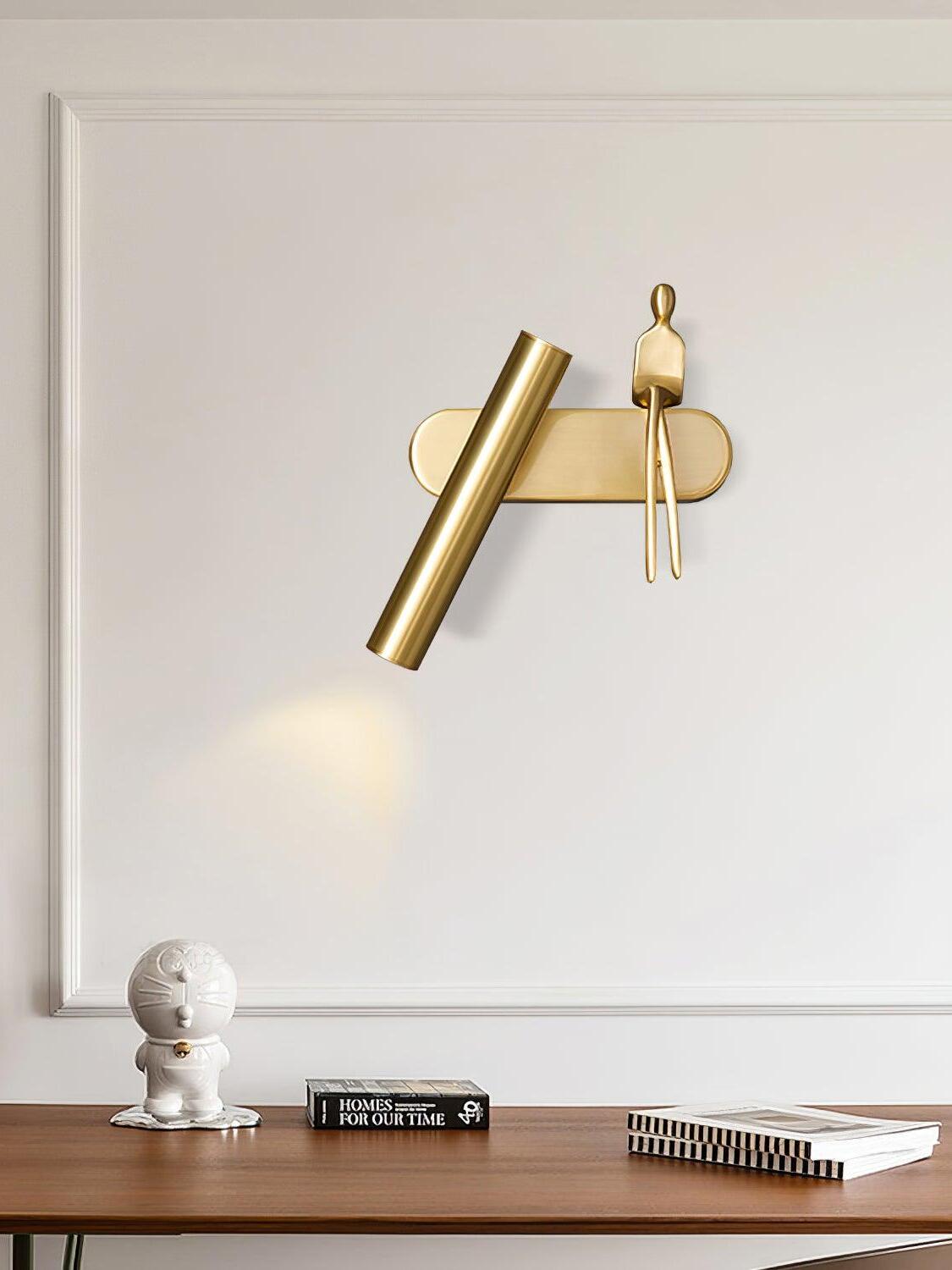 Brass-coloured tube light and seated figure above a console with books and a white sculpture