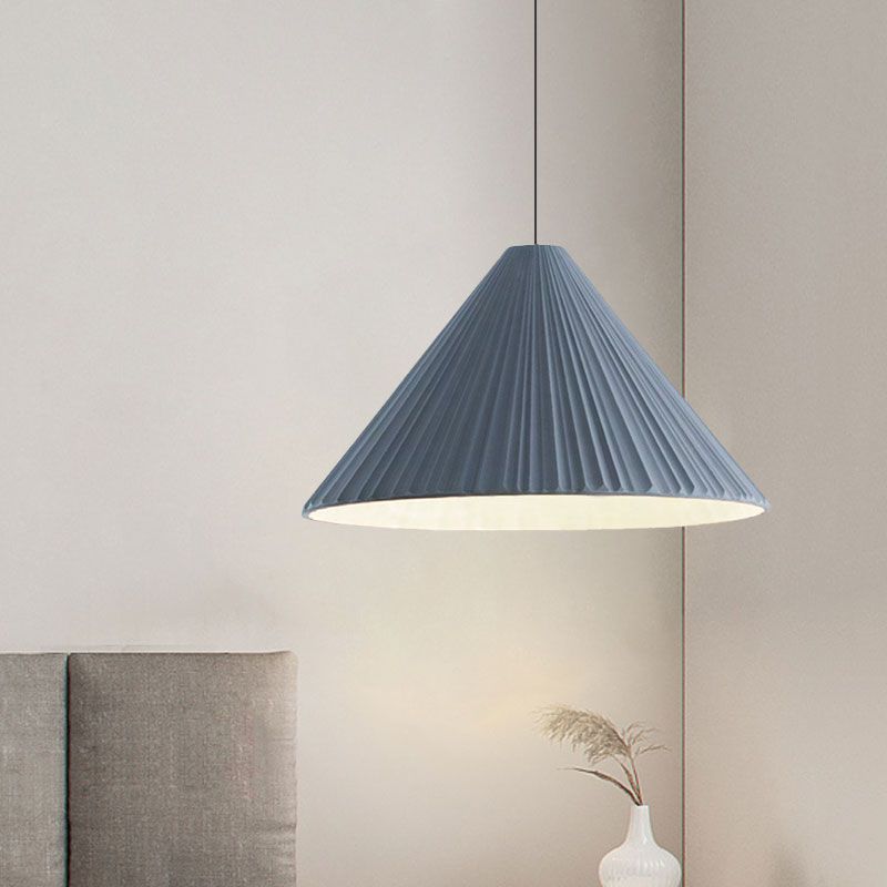 Blue taller pleated cone pendant with a pale underside beside a gray upholstered headboard