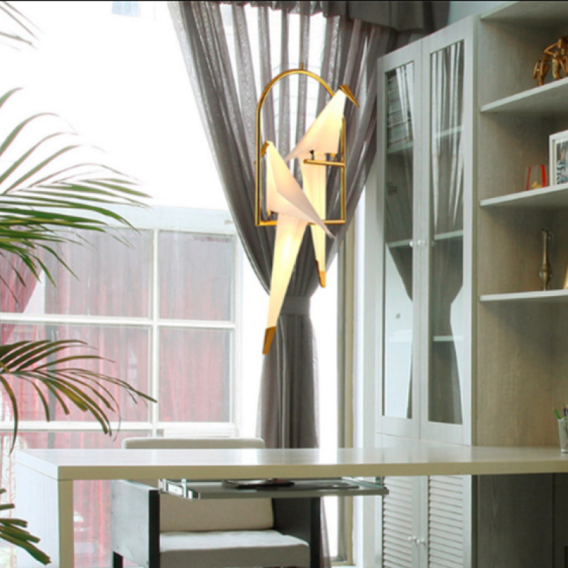Two-bird pendant hanging beside curtains and a tall leafy plant.