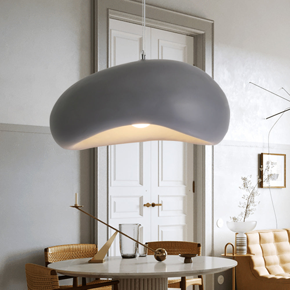 Gray Byers curved pendant light above a round table with woven chairs and a decorative balance object, in front of white double doors.
