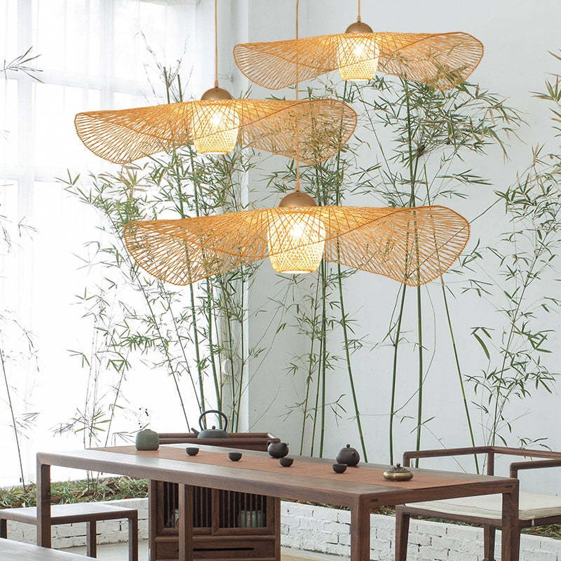Three wavy woven pendants above a wood tea table with chairs, bamboo plants and a bright window
