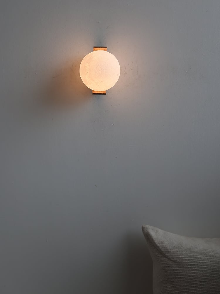 Front view of a glowing moon globe with wood bracket tips above and below on a pale wall