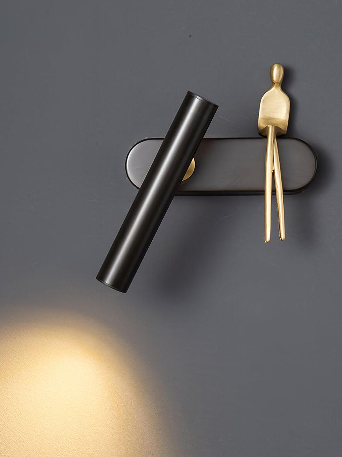 Front view of black tilted tube with seated gold figure on the right and light falling below