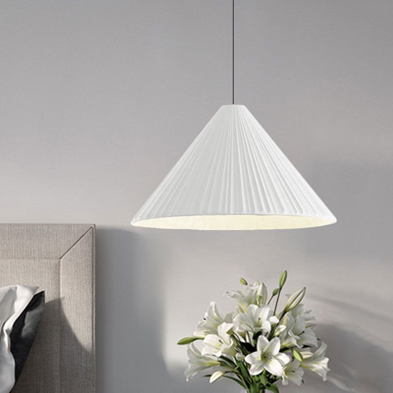 White taller pleated cone pendant beside a gray headboard and white lilies