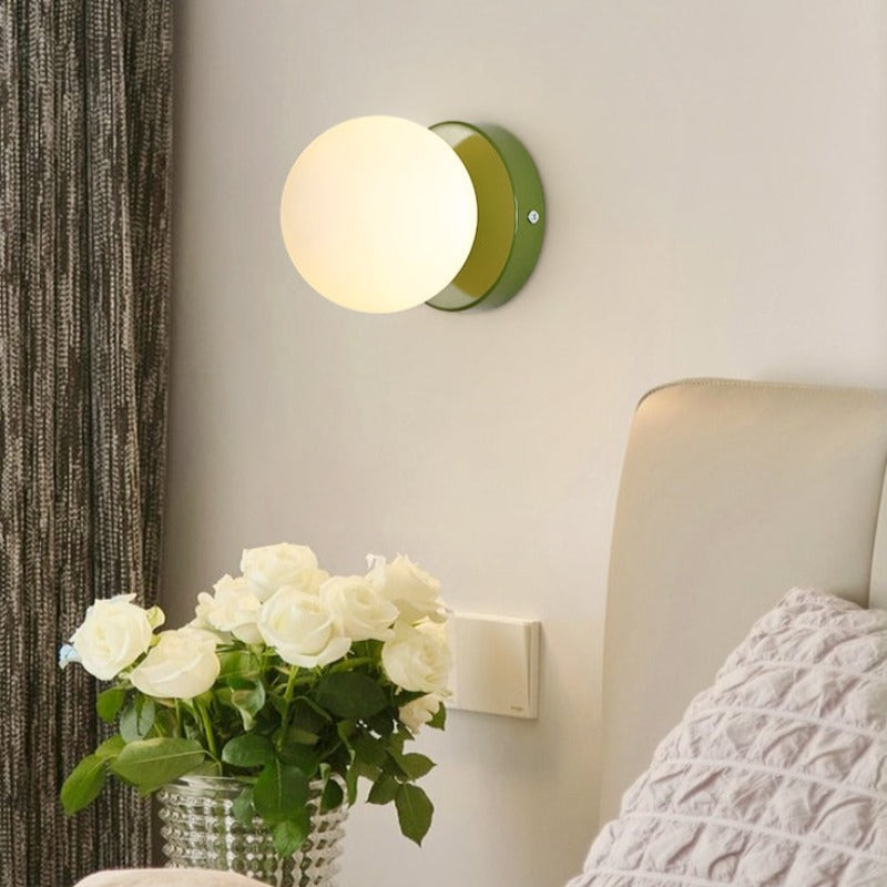 Green globe wall sconce lit beside a bedroom bed