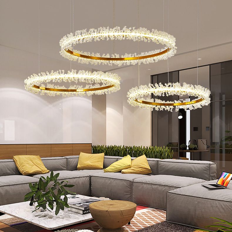 Three gold-tone Kristy flower rings suspended above grey seating, yellow cushions and a round coffee table.