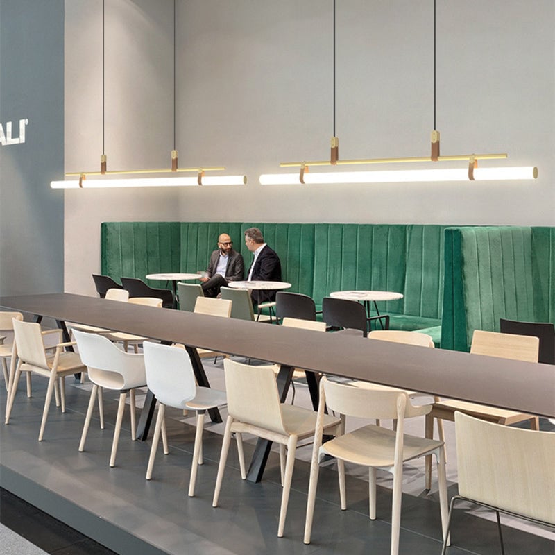 Two separate Gold linear pendants above a communal table with white wooden chairs and a green cafe banquette