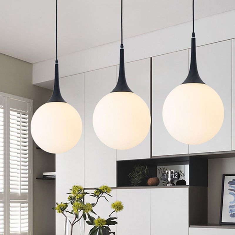Three glowing white Valentina globes with black tapered necks above flower vase and cabinets beside window shutters