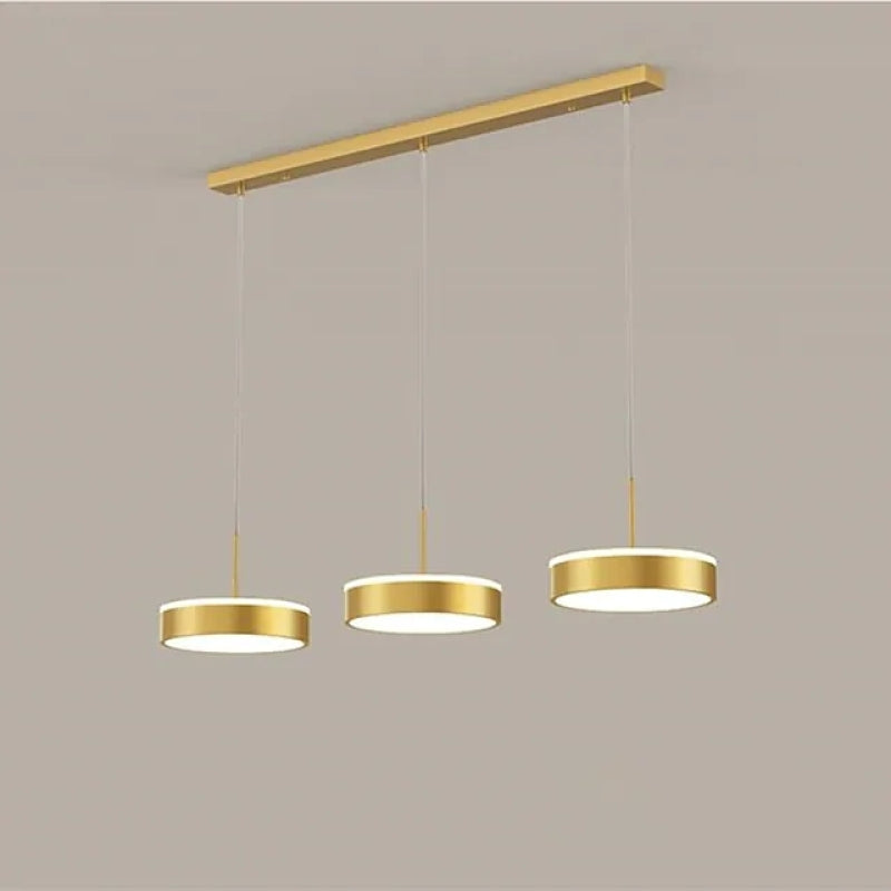 Gold Raheel three-disc pendant against a plain wall.