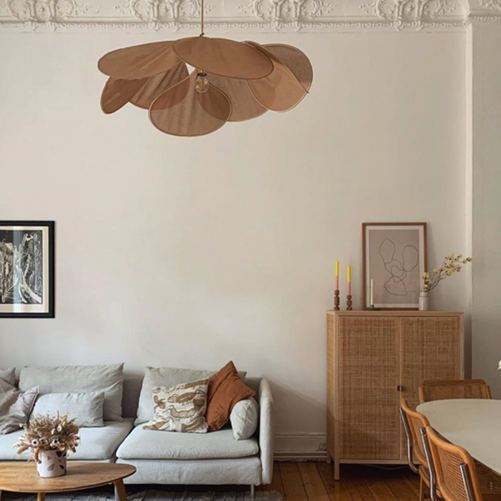 Brown Renée over a pale sofa and oval coffee table, beside a cane-front cabinet with yellow candles and framed artwork.