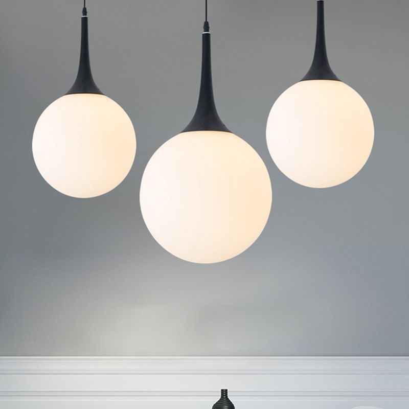Three glowing white Valentina globes with black necks at staggered heights against grey wall with white moulding