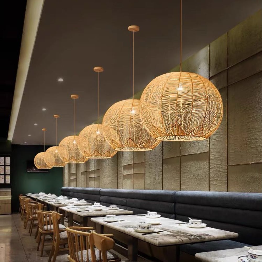 Row of Ritta woven pendants above restaurant tables with tea cups, wooden chairs and a dark upholstered banquette.