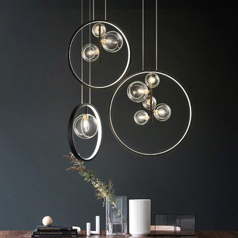 Three separate black ring pendants with clear globes above a wood surface with books and vases