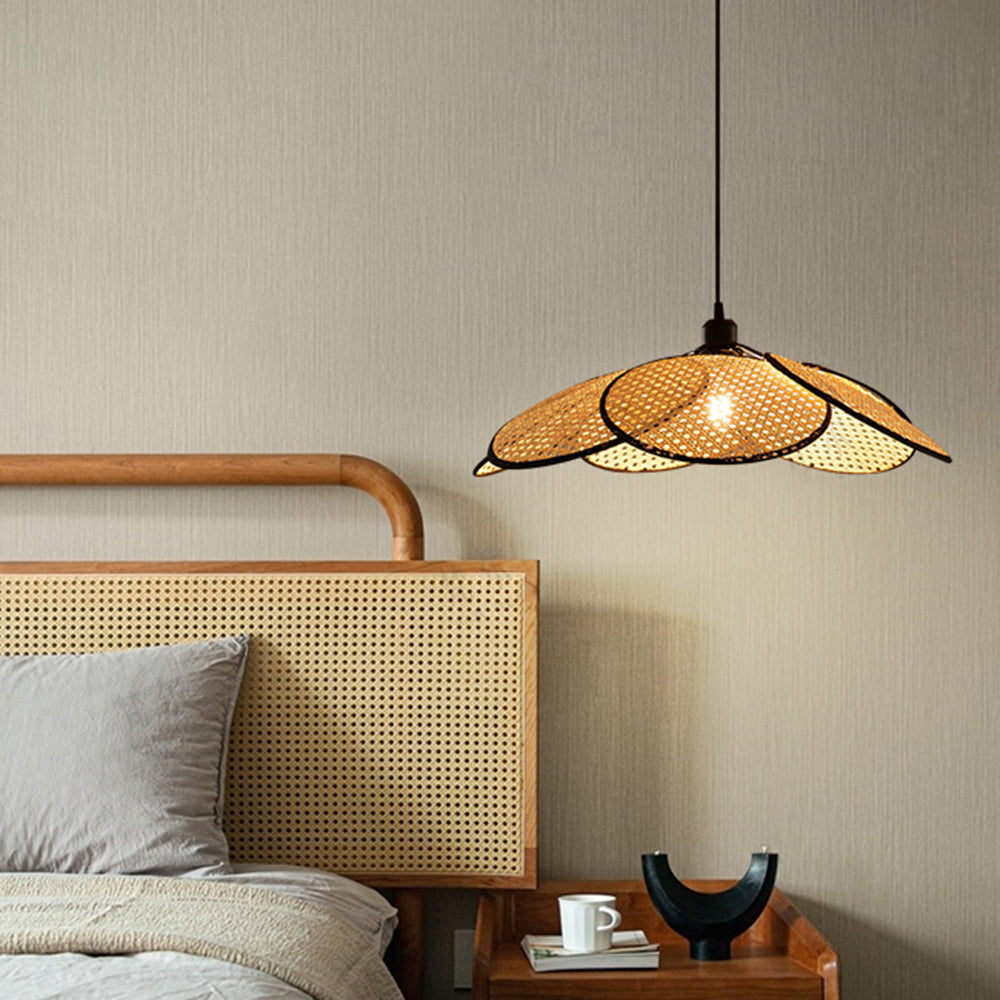 Black-trim Ritta pendant lit beside a woven headboard, gray bed pillow and wooden bedside table with cup and books