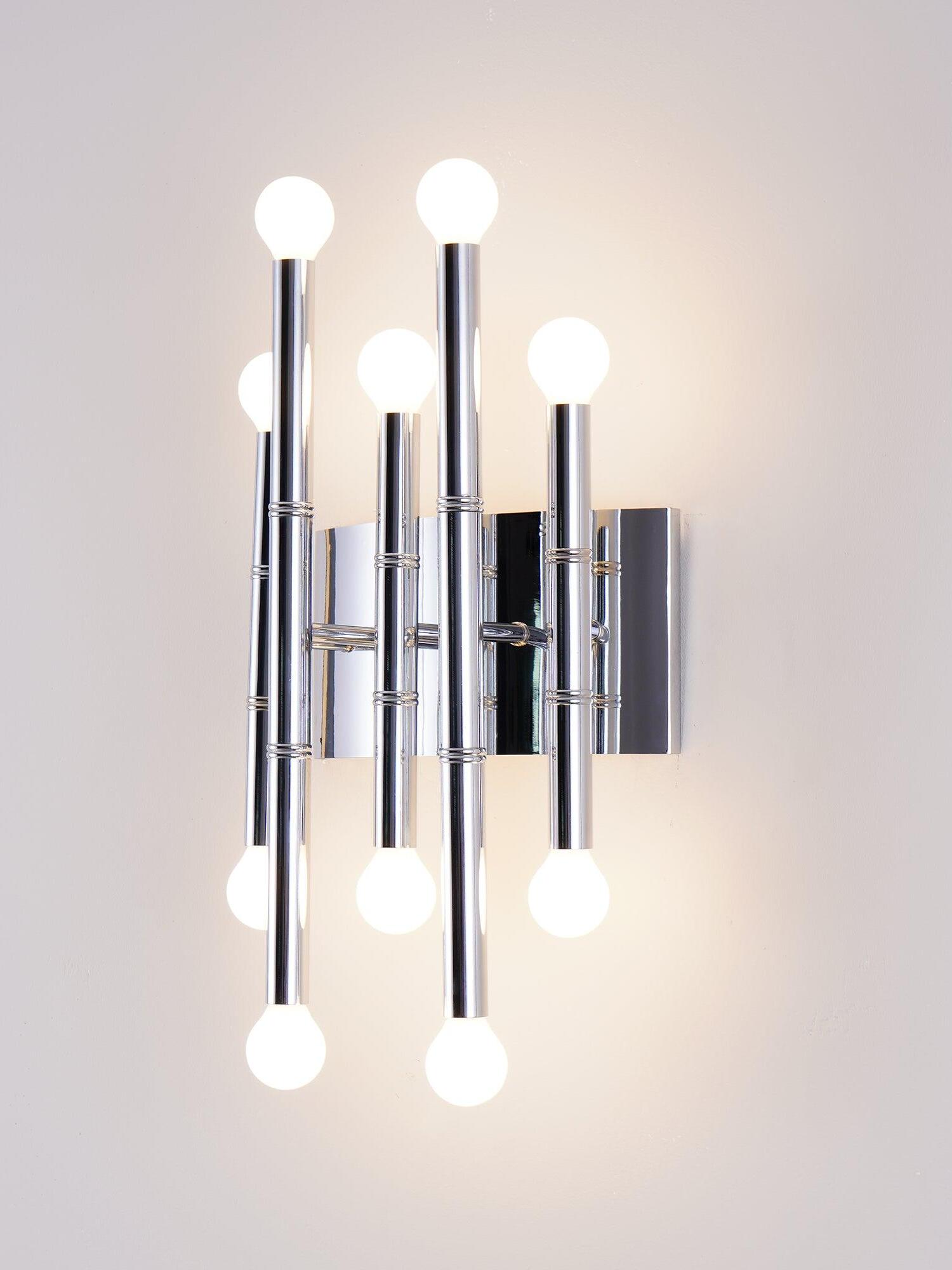 Close angled view of Chrome Meurice with staggered shiny metal stems, lit globe bulbs and a reflective backplate