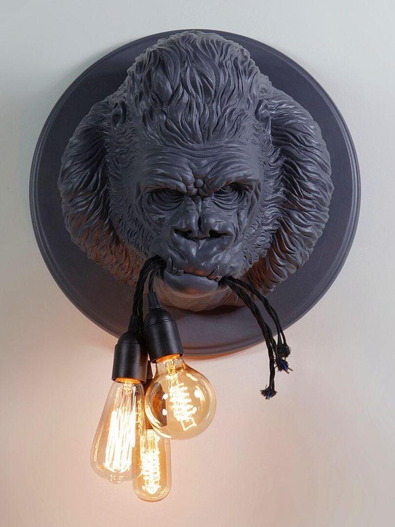 Grey gorilla head and three glowing elongated bulbs against pale wall