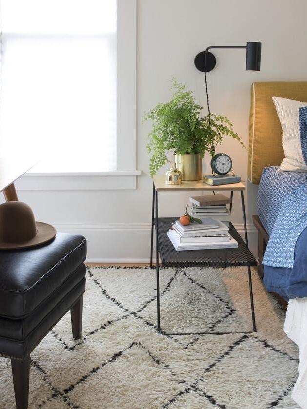 Black wall light above nightstand with greenery and blue bedding