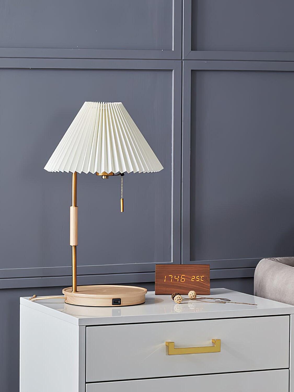 White pleated lamp with a light wood base on a white two-drawer cabinet against a grey panelled wall