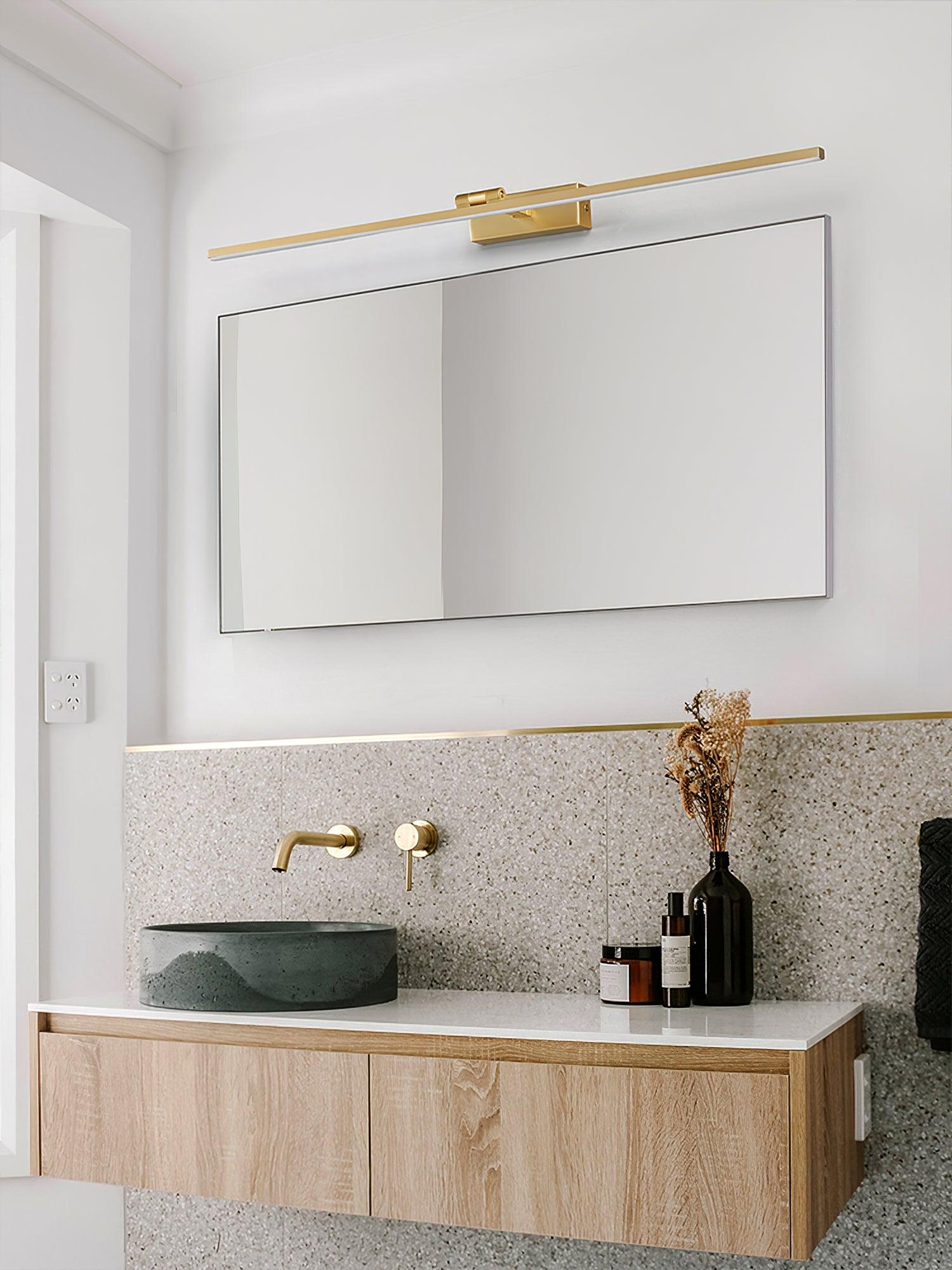 Gold-tone linear wall light above rectangular mirror, green bowl basin and oak cabinet against speckled backsplash