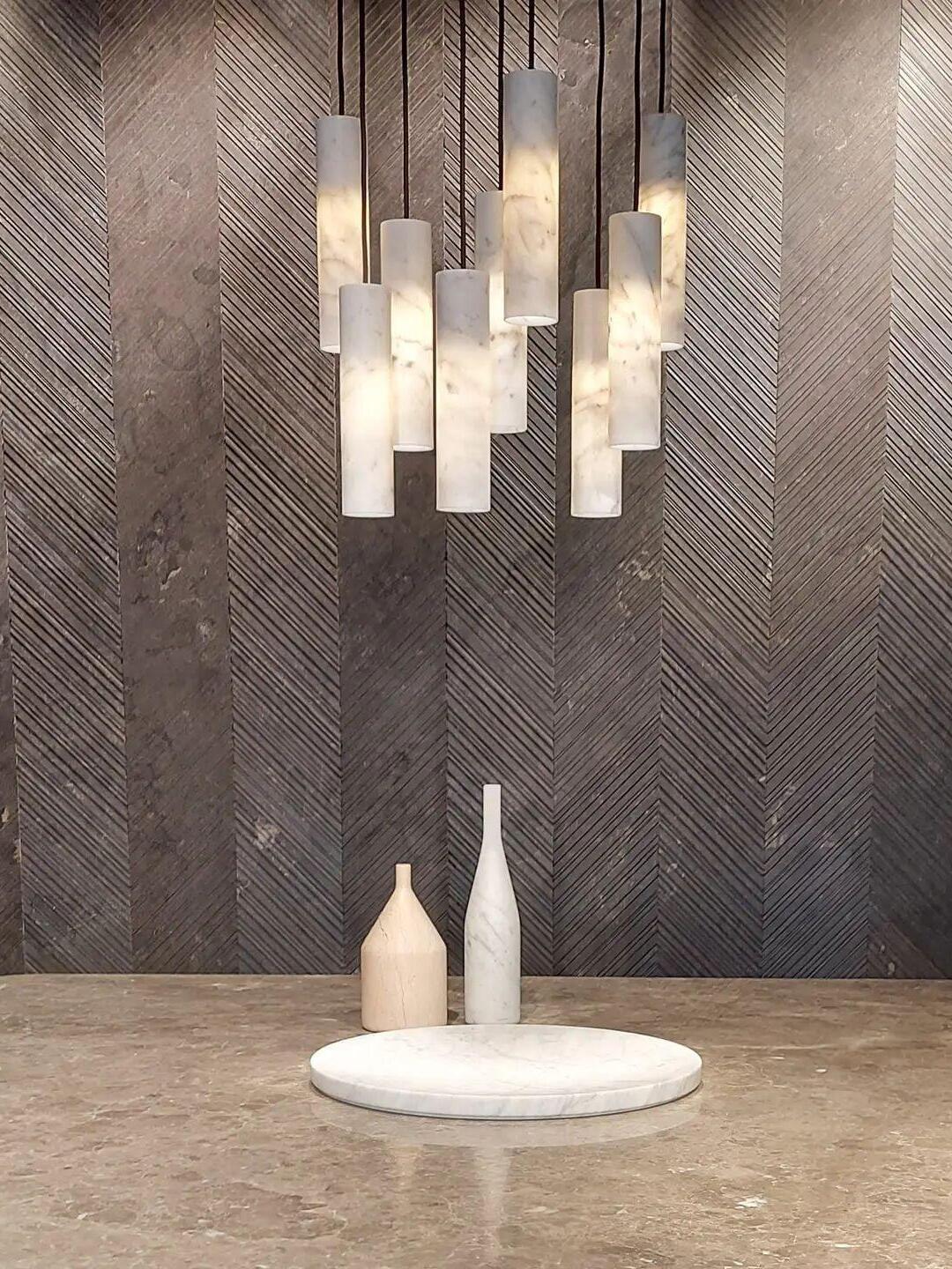 Illuminated Silo cylinders above two pale vases and a white tray against a patterned dark wall