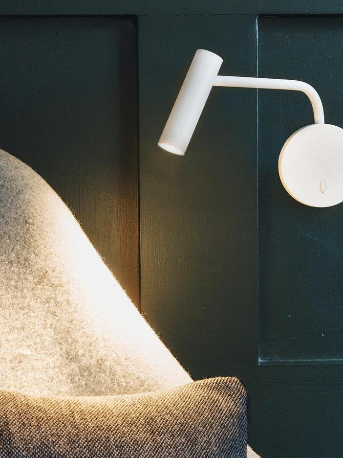 White L-arm wall light beside a lounge chair