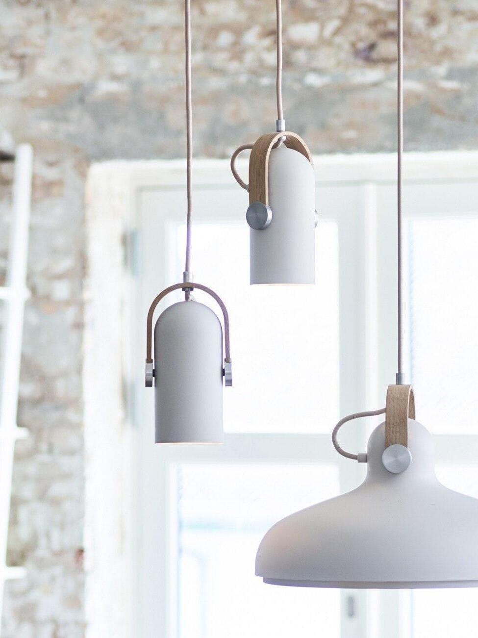 Two small white cylindrical pendants with wood brackets beside a larger flared white pendant, against brick and windows