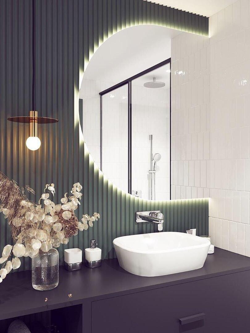 Close view of brass-tone disc pendant beside curved illuminated mirror, green ribbed wall and white basin