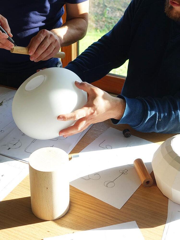 Hands holding a white glass shade beside lighting parts