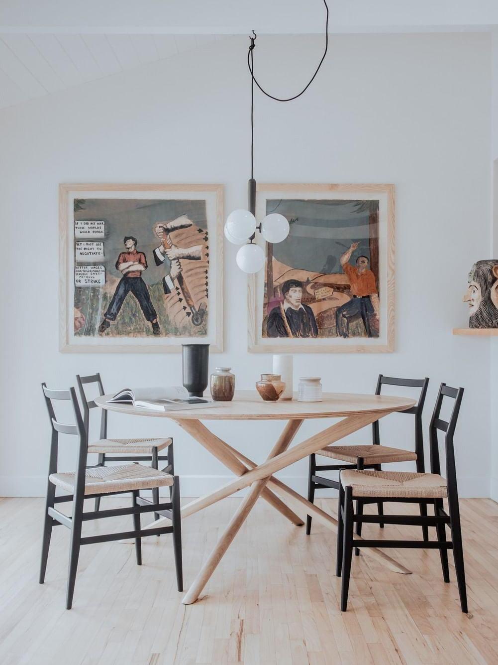 Three white globes on a gray-looking stem above a round wooden table and framed illustrations