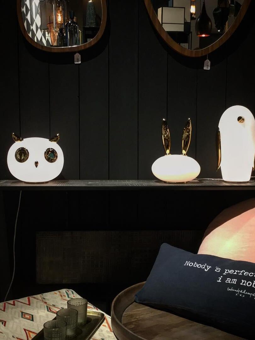 Owl, rabbit and penguin on dark console beneath round mirrors