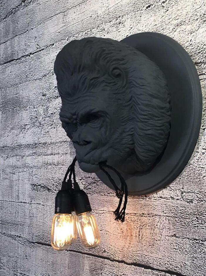 Dark grey gorilla relief on pale brick wall with black cords and glowing bulbs