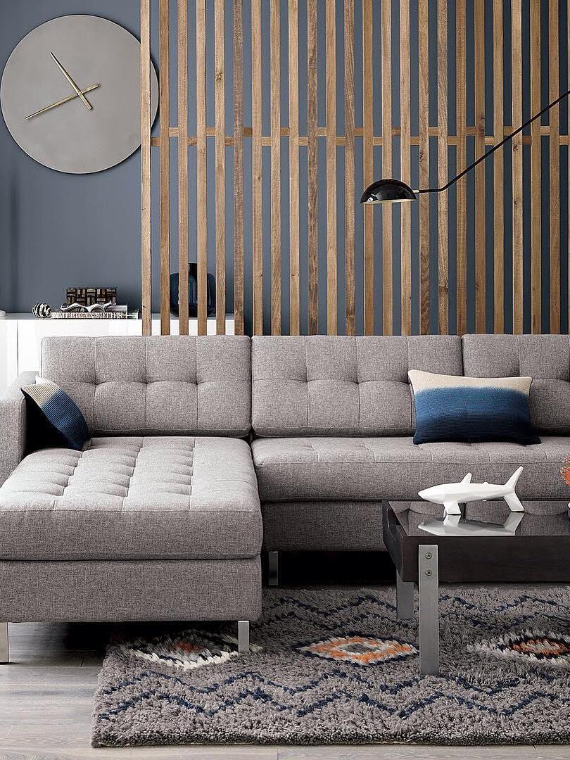 Black dome wall lamp extending above a grey sectional sofa with blue cushions, wood-slat wall and round clock